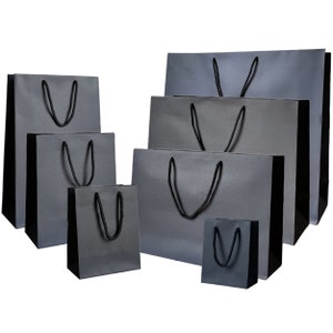 May include: A set of seven black paper gift bags of varying sizes with black handles. The bags are arranged in a staggered formation, with the largest bag at the top and the smallest bag at the bottom.