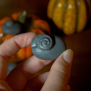 Peut inclure: Une main tenant une petite sculpture en céramique grise d'un bélier avec une corne en spirale. La sculpture est nette, tandis que l'arrière-plan est flou et hors de portée.