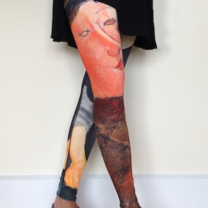 May include: A pair of black leggings with a colorful painting of a woman's face on the right leg and a painting of a woman's torso on the left leg.