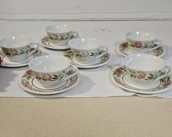 May include: Set of six white teacups and saucers with floral designs. The cups and saucers feature pink and green floral patterns.