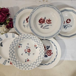 Peut inclure: Ensemble de six bols à soupe en céramique blanche avec des motifs floraux et géométriques. Les bols présentent des motifs floraux rouges et bleus, avec des bordures festonnées, à carreaux et à rayures. Les bols sont disposés sur une surface blanche.
