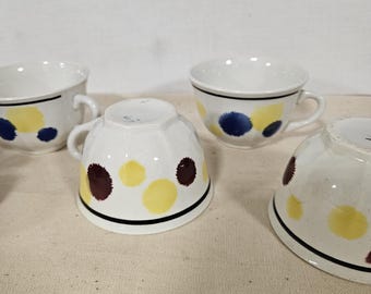 May include: Set of four white ceramic coffee cups with a black rim. Each cup has a different pattern of yellow, blue, and brown polka dots.