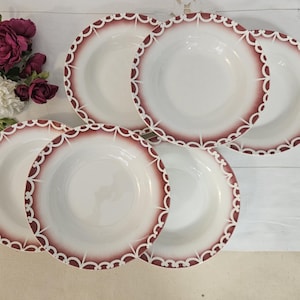 Op de afbeelding: Zes witte keramische kommen met een geschulpte bordeauxrode en witte rand. De kommen zijn gerangschikt op een wit oppervlak, met bordeauxrode en witte bloemen op de achtergrond. Een set elegant servies.