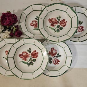 Peut inclure: Ensemble de six assiettes en céramique blanche avec une bordure géométrique verte et un motif floral central de roses rouges et de feuilles vertes. Les assiettes sont disposées avec un bouquet de fleurs.