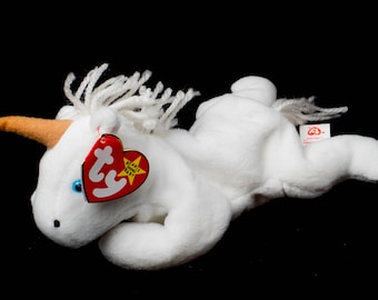 Könnte beinhalten: Weißes Plüsch-Einhorn-Spielzeug mit einem roten und weißen Beanie Baby-Etikett, auf dem "Beanie Babies" und ein gelber Stern stehen. Das Einhorn hat ein braunes Horn und blaue Augen.