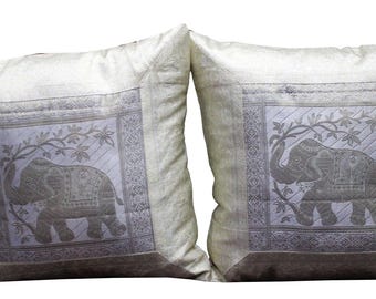 May include: Two off-white throw pillows with embroidered silver elephant designs. The elephants are standing on a branch with leaves and are surrounded by a silver border.