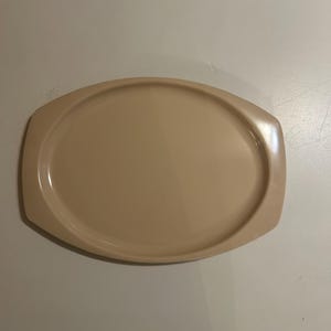 May include: A solid light beige oval serving platter with a smooth, glossy finish. The platter features a wide, flat rim on both the left and right sides, providing integrated handles for easy gripping and a central recessed area for food.