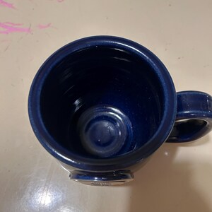Może przedstawiać: Kubek ceramiczny w ciemnoniebieskim kolorze z srebrną obw&oacute;dką i srebrnym logo na spodzie.