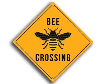 May include: A yellow diamond-shaped sign with a black bee illustration and the words "BEE CROSSING" in black capital letters. The bee has a honeycomb pattern on its body and wings.
