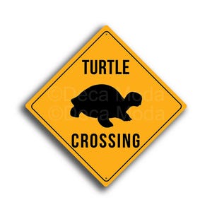 Può includere: Segnale stradale giallo a forma di diamante con una silhouette di tartaruga nera e le parole "TURTLE CROSSING". Il segnale avverte i conducenti delle tartarughe.