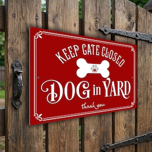 May include: A red metal sign with white text that reads "KEEP GATE CLOSED DOG in YARD thank you." The sign features a white bone with a gray paw print. The sign is mounted on a wooden gate.