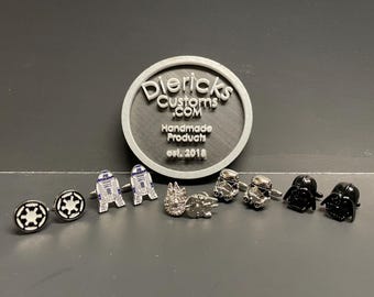 May include: A set of eight silver cufflinks featuring Star Wars characters. The cufflinks include Darth Vader, Stormtroopers, R2-D2, and the Death Star. The cufflinks are displayed on a black surface with a white logo that reads "Diericks Customs.com Handmade Products est. 2016".