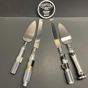 May include: Four silver cake servers with black and silver handles. The handles are designed to look like lightsabers. The servers are arranged in a row on a gray surface.