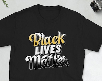 Puede incluir: Camiseta negra con el texto "Black Lives Matter" en una fuente estilizada y en capas con acentos dorados y blancos.