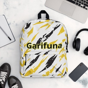 May include: A white backpack with a black and yellow abstract pattern. The backpack has a zippered pocket on the front and the word "Garifuna" printed in yellow with a black outline.