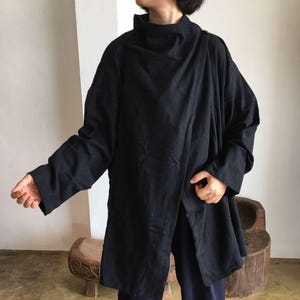 Puede incluir: Una chaqueta negra de manga larga con cuello alto y diseño drapeado. La chaqueta está hecha de una tela suave y texturizada.