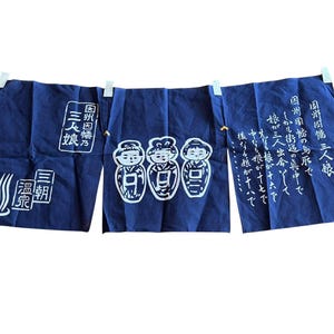 Könnte beinhalten: Ein marineblauer japanischer Noren-Vorhang mit weißen Illustrationen und Text. Der Vorhang ist in drei Paneele unterteilt, jedes mit einem einzigartigen Design. Das linke Paneel zeigt ein stilisiertes Thermalbad-Design und japanischen Text. Das mittlere Paneel zeigt drei Figuren.