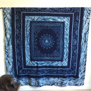 Könnte beinhalten: Eine große indigoblaue Baumwoll-Wandbehang mit einem weißen Stickmuster. Das Design zeigt eine zentrale Blume mit einem sich wiederholenden Muster aus Blättern und Spiralen.