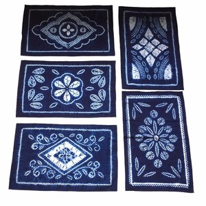 Puede incluir: Cinco cuadrados de tela azul índigo con patrones de teñido anudado blancos. Cada cuadrado presenta un diseño diferente, que incluye una flor, un diamante y formas geométricas.