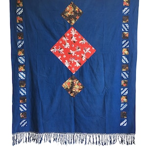 Puede incluir: Una manta de algodón azul con un diseño de patchwork. La manta tiene un borde de flecos y presenta un patrón de diamante con tela roja, blanca y negra.