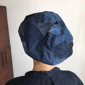 Op de afbeelding: Een blauwe denim-beret gemaakt van patchwork-stof. De beret is gemaakt van verschillende tinten blauw denim en heeft een licht afgeronde vorm.