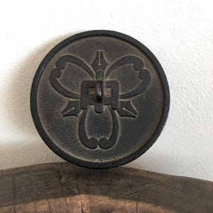 May include: A round black cast iron ornament with a decorative floral design. The ornament has a small metal loop on the top.