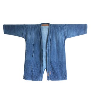 Könnte beinhalten: Blaue Jeans-Kimono-Jacke mit langen Ärmeln. Die Jacke hat ein Rautenmuster am Saum und ein strukturiertes Design. Sie wird auf einem Holzbügel vor weißem Hintergrund präsentiert.