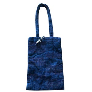 Könnte beinhalten: Eine blaue Tragetasche mit einem strukturierten Muster und einem passenden Griff. Die Tasche hat einen Kordelzugverschluss mit einer weißen Kordel. Die Tragetasche ist aus einem gewebten Stoff gefertigt.