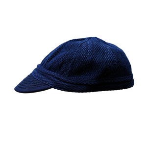 Puede incluir: Gorra de estilo newsboy en azul marino con un diseño de punto texturizado. La gorra presenta una visera corta y curvada y una corona redondeada. La tela parece ser un material tejido apretado, que ofrece un aspecto clásico y elegante. Este sombrero es un accesorio versátil.