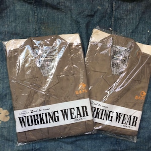 May include: Two brown shirts with white collars and a white trim on the sleeves. The shirts are packaged in plastic and have the text "Working Wear - Tokyo" on the front. The shirts also have a small logo with the text "BATIV" on the front.