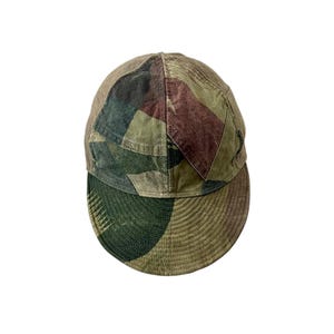 Op de afbeelding: Een baseballpet met een patchworkontwerp van verschillende camouflagepatronen in tinten olijfgroen, bruin en beige. De pet heeft een ronde kroon en een gebogen klep met zichtbare cirkelvormige stiksels over het gehele stoffen oppervlak.