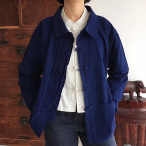 Puede incluir: Chaqueta azul marino con cuello mandarín y cierres de rana. La chaqueta tiene dos bolsillos delanteros y se usa sobre una camisa blanca con cierres de rana similares. La chaqueta es de corte holgado.