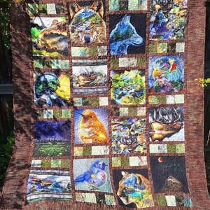May include: A large, quilted blanket featuring a patchwork design with images of wildlife. The squares depict a wolf, a duck, a bird, and a deer, among others. The quilt has a brown border and is displayed outdoors.