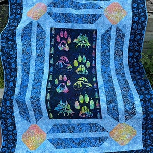 May include: A blue and black quilt with a pattern of paw prints and trees. The quilt is made of fabric with a batik design.