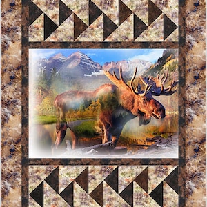 May include: A decorative quilt featuring a majestic moose standing in a lake with mountains in the background. The quilt has a brown and tan border with geometric triangle patterns. The central image is a scenic landscape.