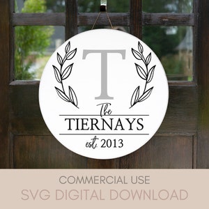 Peut inclure: Panneau rond en bois blanc avec la lettre "T" grise et le nom de famille "The Tiernays" en noir. Le panneau est orné de branches de feuilles noires et de l'année "est. 2013". Il est suspendu à une ficelle marron.