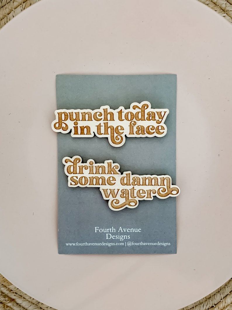 May include: Two wooden signs with motivational phrases in a retro font. The top sign reads "punch today in the face" and the bottom sign reads "drink some damn water".