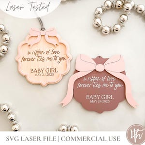 Puede incluir: Dos adornos de madera cortados con láser para bebé niña con diseño de lazo. Los adornos son de color rosa claro y marrón, con el texto "a ribbon of love forever ties me to you" y "BABY GIRL MAY 24 2025".