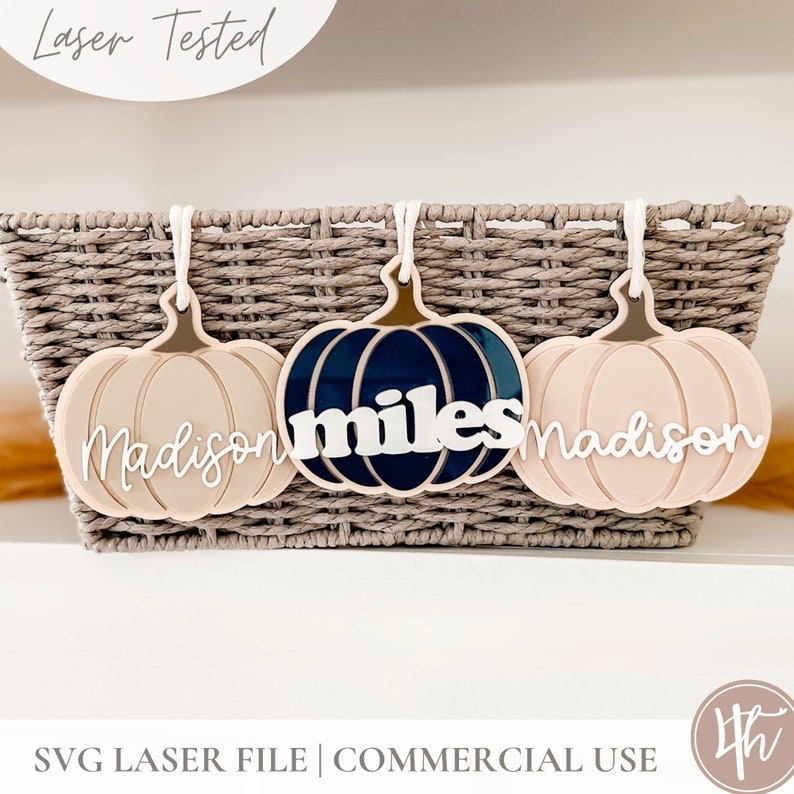 May include: Three pumpkin-shaped ornaments with the names "Madison", "miles", and "Madison" written on them. The pumpkins are in a wicker basket. The pumpkins are pink and blue.