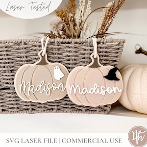 May include: Two beige pumpkin-shaped ornaments with the name "Madison" written on them. One pumpkin has a white ghost and the other has a black witch's hat.