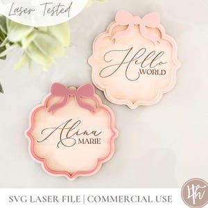 Puede incluir: Dos letreros de madera cortados con l&aacute;ser con un dise&ntilde;o de lazo rosa. El letrero superior dice "Hello World" y el letrero inferior dice "Alina Marie".