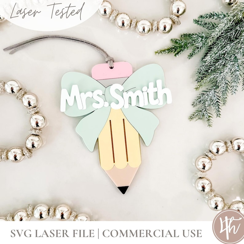 May include: A pastel-coloured pencil-shaped ornament with a bow and the name "Mrs. Smith" in white. The ornament has a pink top, a light blue bow, and a yellow pencil body with a pink tip and black point. The text "Laser Tested" is in the upper left.