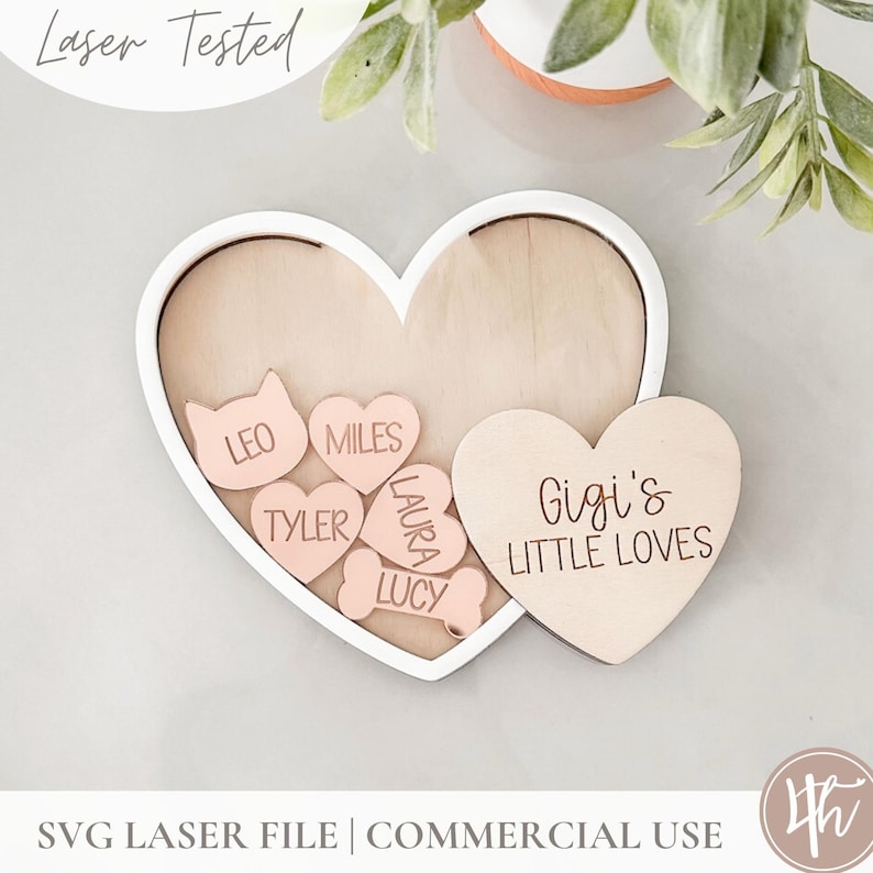 May include: A white heart-shaped frame with a smaller heart-shaped frame inside. The smaller frame has the text "Gigi's Little Loves" engraved on it. The larger frame contains several smaller hearts with names engraved on them, including "Leo", "Miles", "Tyler", "Laura", and "Lucy".