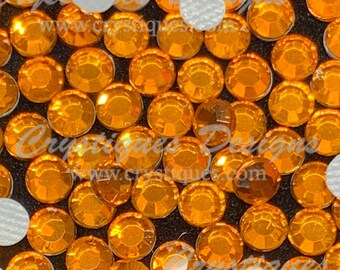May include: Close-up of a large quantity of orange rhinestones, some with adhesive backing, scattered on a black surface.