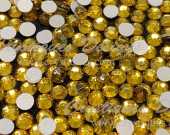 May include: A close-up image of a large quantity of gold-colored rhinestones. The rhinestones are scattered on a black surface.
