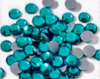 May include: A large quantity of teal blue round rhinestones. The rhinestones are scattered on a white surface.