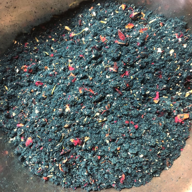 May include: A close-up of a dark blue powder with red and white flower petals mixed in. The powder is in a bowl.