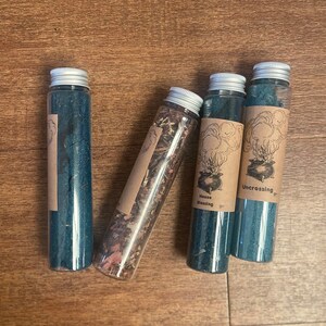 May include: Four glass bottles with cork tops and labels. The labels are brown with black text and illustrations. The bottles contain blue and brown liquids. The labels read "House Blessing", "Uncrossing", and "Uncrossing".