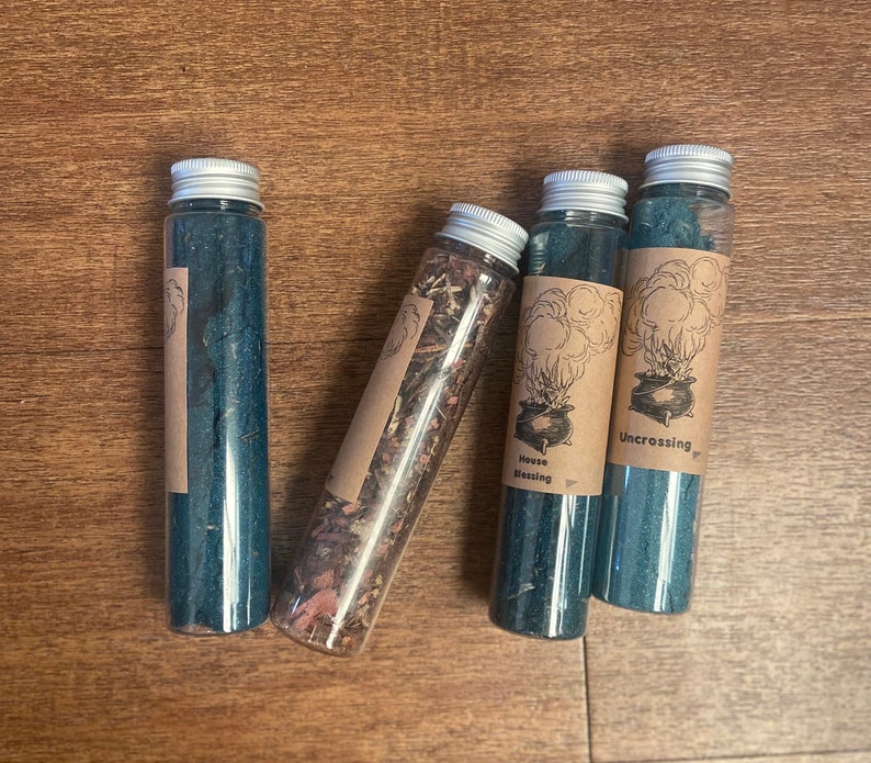 May include: Four glass bottles with cork tops and labels. The labels are brown with black text and illustrations. The bottles contain blue and brown liquids. The labels read "House Blessing", "Uncrossing", and "Uncrossing".