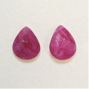 Puede incluir: Par de piedras preciosas rosadas en forma de pera con un corte facetado. Las piedras preciosas son translúcidas y tienen un aspecto ligeramente nublado.